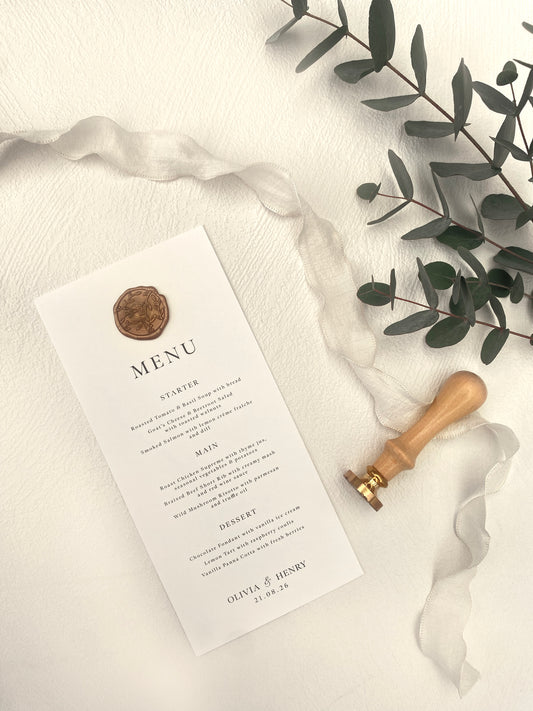 Menu card with a seal on a white fabric background with greenery