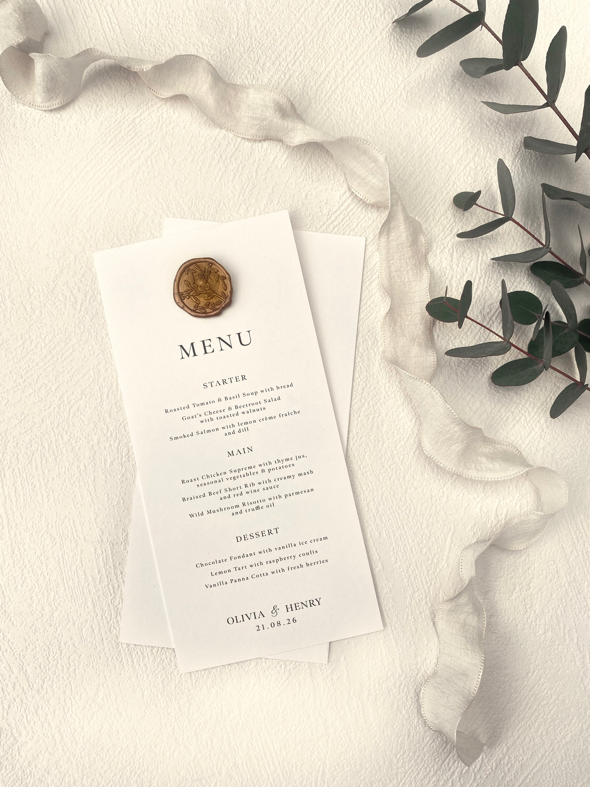Wedding menu card with a wax seal on a textured surface with greenery