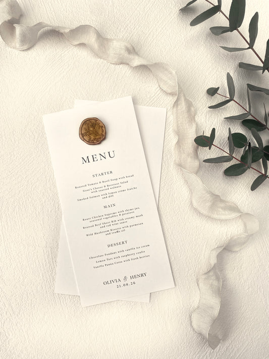 Wedding menu card with a wax seal on a textured surface with greenery