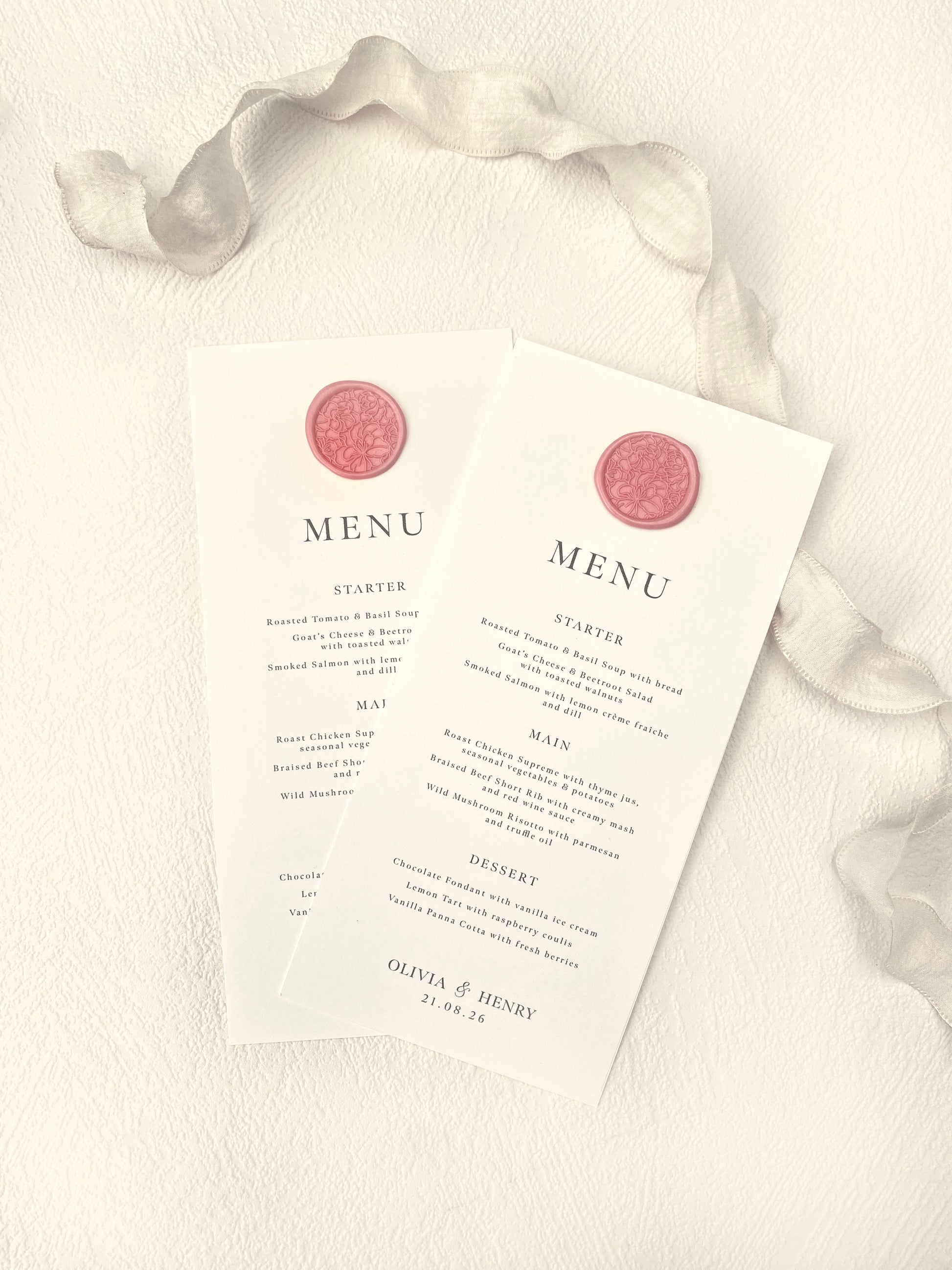 Two menu cards with a pink wax seal design on a textured white surface